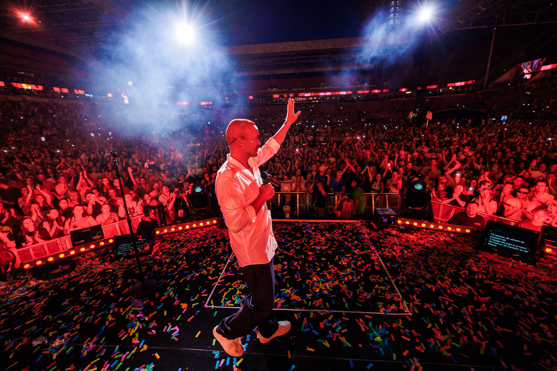 Artiest op een podium vol confetti voor een uitzinnig publiek in rood licht